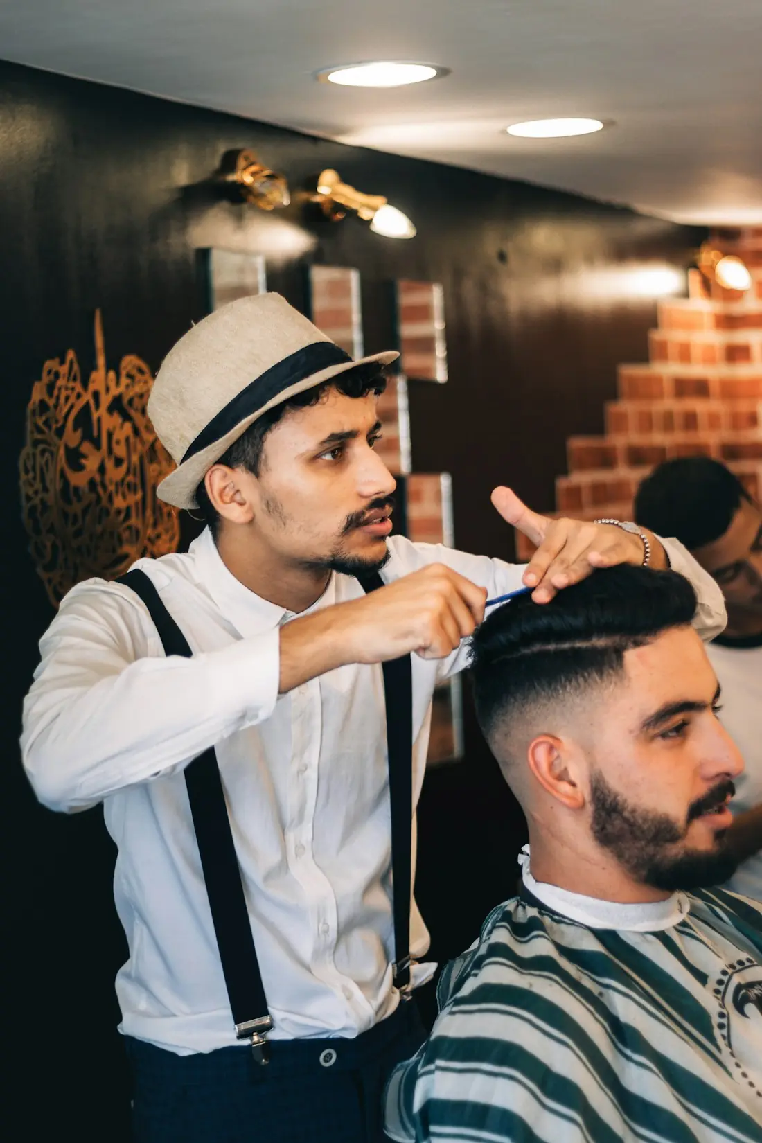 A barber in a hat fading a client's sides
